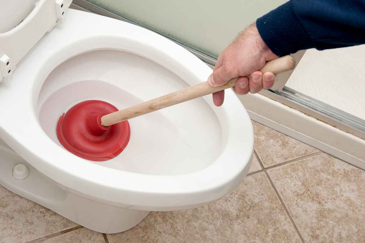 A plumber uses a plunger to unclog a toilet.