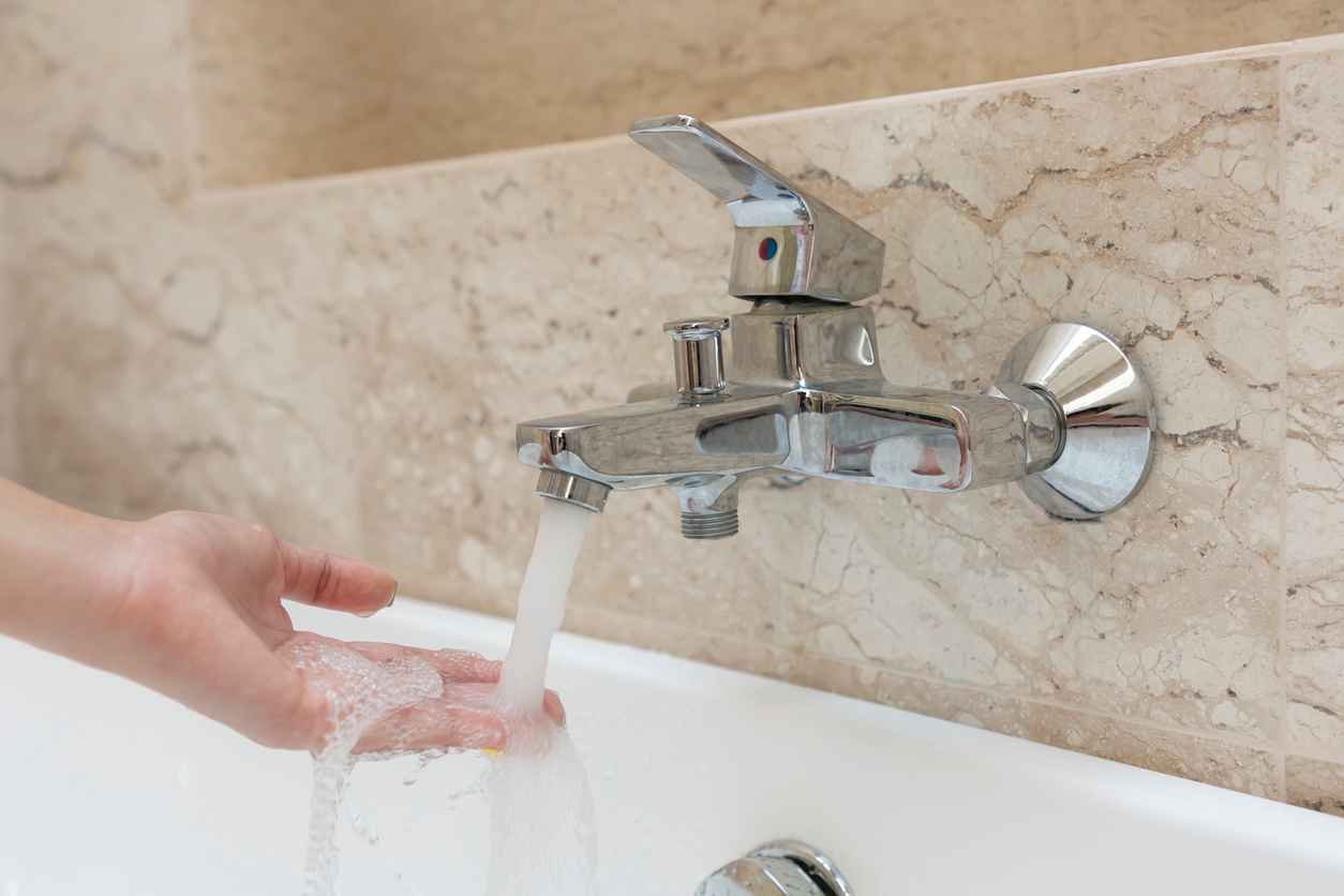 A woman checking the water temperature from the bathtub faucet with her hand