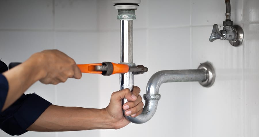Plumber using wrench and tools to open a pipe under the sink