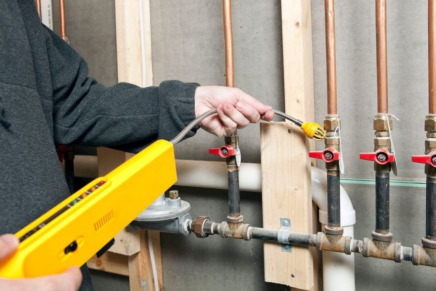 A worker is using a leak detector near a set of house gas lines at a renovation site
