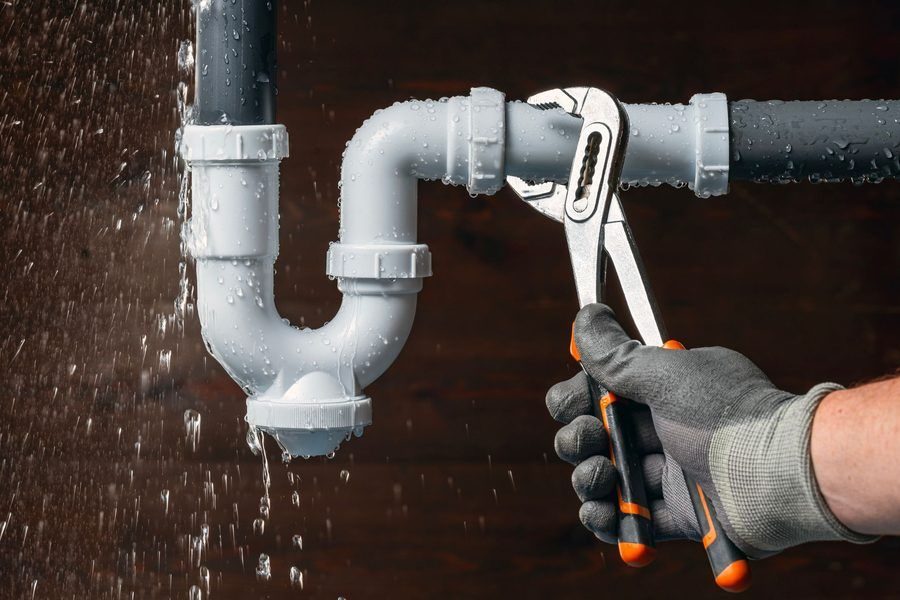 plumber's hand in a glove with a wrench repairing a leaking PVC pipe