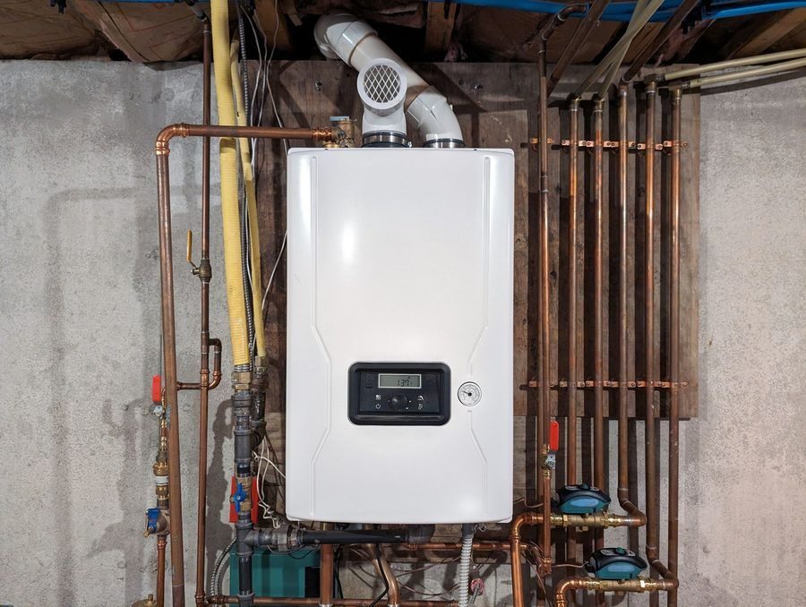 white tankless water heater and piping on a concrete wall