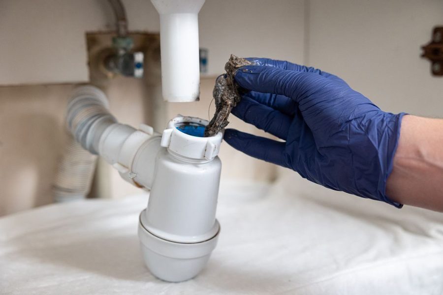 plumber's hand clearing a drain pipe of a hair clog