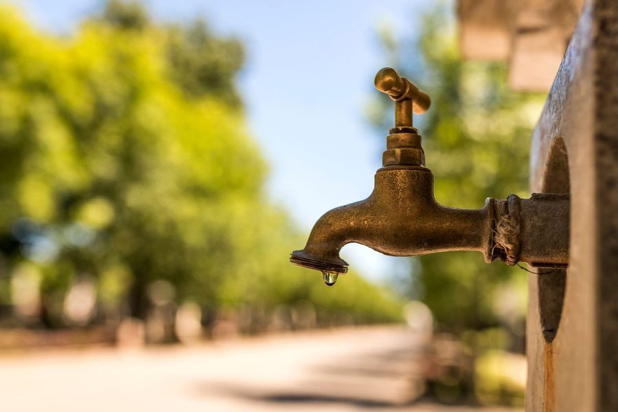 old and used water faucet leaking with dripping drops during bright, hot sunny day