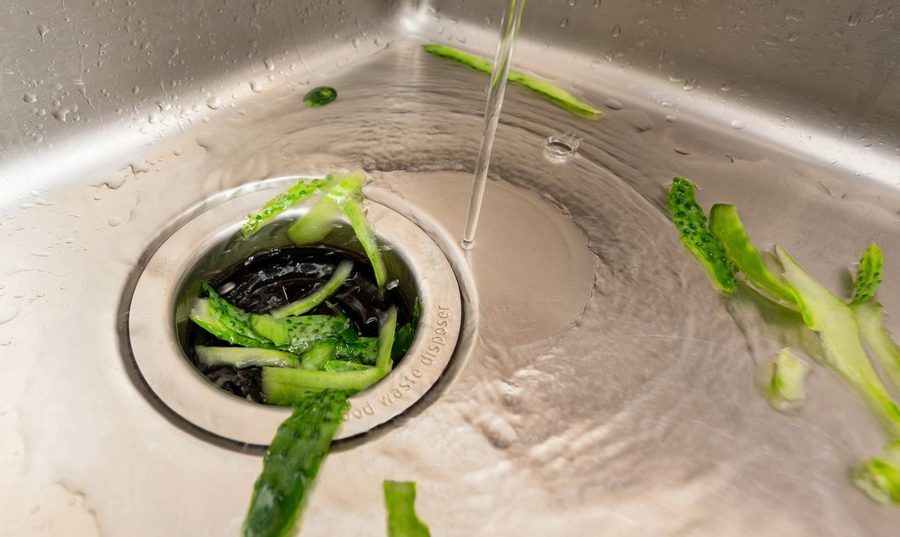 Efficient kitchen waste disposal system handling cucumber peels with running water in a modern sink setup